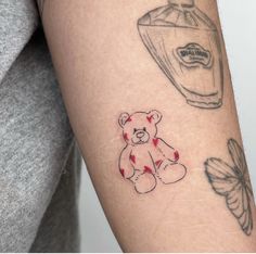 a person with a tattoo on their arm has a teddy bear next to a bottle