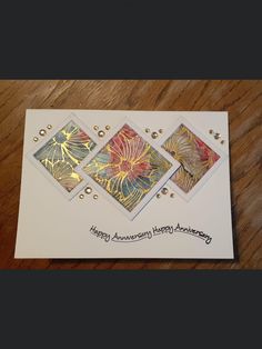 an anniversary card with gold and red flowers on white paper, sitting on a wooden table