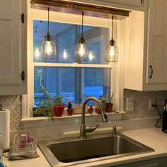 a kitchen sink under a window with lights hanging from it's windowsill and potted plants on the counter