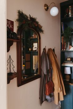 a coat rack with coats hanging on it next to a mirror and bookshelf