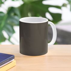 a black and white coffee mug sitting on top of a wooden table next to a book