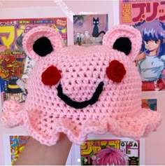 a pink crocheted bear with black eyes and nose is held up by someone's hand