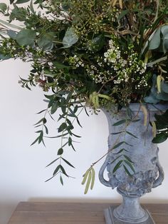 a vase filled with lots of greenery on top of a table