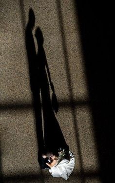 the shadow of a person standing next to a woman in a wedding dress and holding a bouquet