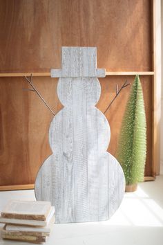 a snowman made out of wood sitting next to a green plant and some books