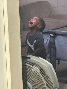 a young boy standing next to an air conditioner and looking up at the ceiling