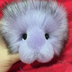 a small stuffed animal is being held by someone's hand on a red blanket