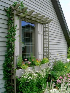 an open window on the side of a house covered in vines and flowers, next to a garden