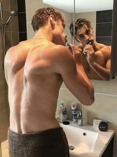 a shirtless man is brushing his teeth in front of a mirror and looking at himself in the mirror