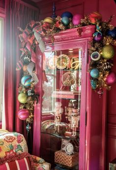 a pink china cabinet decorated with christmas ornaments and ribbon around the top, sitting in a brightly colored room