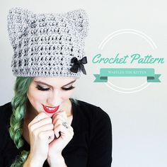 a woman with green hair wearing a crochet cat hat and holding her hands to her face