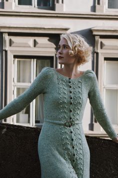 a woman in a green dress leaning against a wall