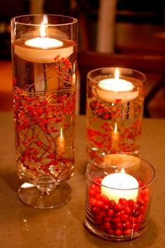 two glass vases filled with red berries and candles