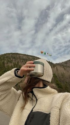 a woman wearing a hat and holding a cup in front of her face while looking up at the sky