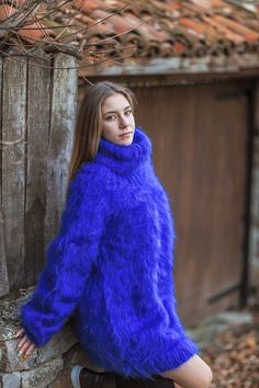 a woman in a blue fuzzy sweater leaning against a wooden fence and posing for the camera