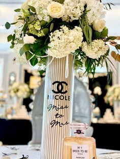 a tall vase with flowers on top of a table next to a bottle of perfume