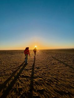 a person walking across a sandy beach at sunset