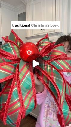 a woman holding a giant christmas bow with a red ball in it's center