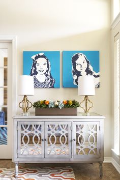 two paintings hang on the wall above a white sideboard in a living room with an orange and blue rug