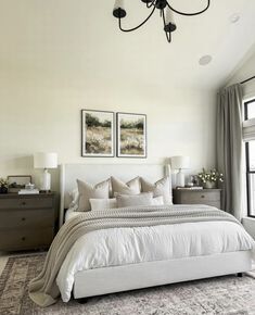 a large white bed sitting under a chandelier in a bedroom next to a window