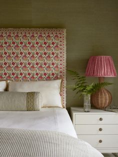 a bed with a pink lamp next to it and a white dresser in the background