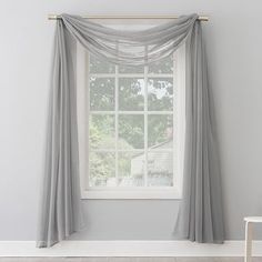 a white chair sitting in front of a window with curtains hanging on the windowsill