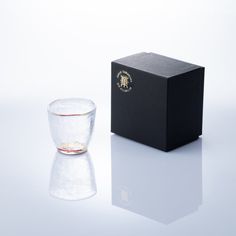 an empty glass next to a black box on a white surface with a reflection in it