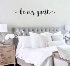 a bed room with a neatly made bed and a wall sticker that says be our guest