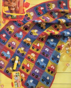 a crocheted blanket with cars and trucks on it, next to a toy truck