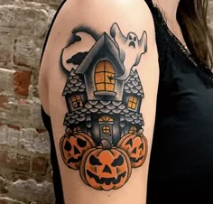 a woman's arm with a house and pumpkins on it, decorated for halloween