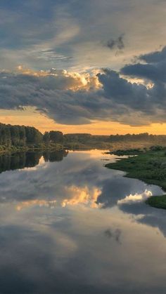 the sky is reflected in the calm water at sunset, with green grass and trees on either side