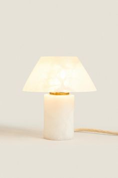 a white table lamp with a light on top of it and a cord attached to the base