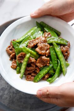 someone is holding a white bowl filled with meat and green beans