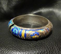 A rare Chinese sterling silver enamel bangle bracelet dating from the Qing Dynasty 1800s. The bangle has beautiful engraving, repousse and chased silver work which has been enameled in areas with cobalt blue, turquoise, and yellow. Minor wear to enamel commensurate with age. Weighs 46.5 grams. Inside diameter 56 mm to fit a small to medium wrist. A very well made and rare piece. Elegant Silver Enamel Bangle, Blue Engraved Jewelry For Ceremonial Occasion, Ceremonial Blue Engraved Jewelry, Blue Ceremonial Bangle Jewelry, Blue Ceremonial Bangle, Blue Ceremonial Bracelet Jewelry, Ceremonial Blue Bracelet Jewelry, Collectible Enamel Bangle Jewelry, Silver Meenakari Bangle Bracelet