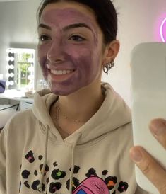 a woman holding up a cell phone with a pink face mask on it's face