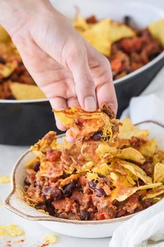 a person scooping some food out of a bowl with tortilla chips on the side