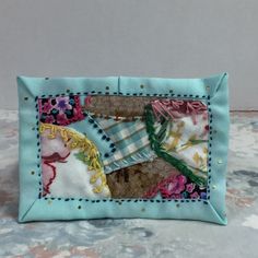 a small purse is decorated with fabric and flowers on the front, along with an embellishment in the middle