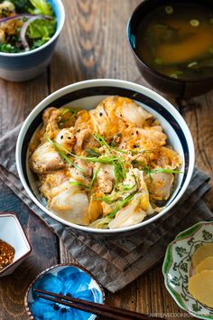 a bowl filled with food next to bowls of soup and chopsticks on a wooden table