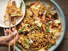 someone is holding chopsticks over a plate of noodles and vegetables with sauce on the side