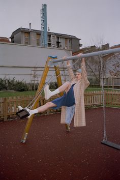 a woman is swinging on a swing set in the playground with her legs spread out