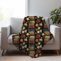 a couch sitting next to a window with a blanket on it that has books and flowers all over it