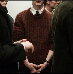 a group of men standing next to each other in front of a mirror wearing sweaters and ties