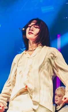 a woman standing on top of a stage with her hands in the air and wearing white clothes