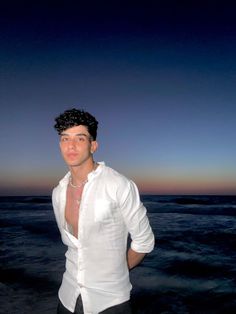 a man standing in the ocean at night with his shirt open and no shirt on