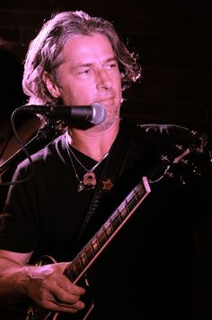 a man that is playing a guitar in front of a microphone