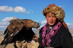 a man with an eagle on his arm in front of the sky and mountains behind him