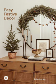 a christmas wreath on top of a dresser next to pictures and candles in front of a mirror