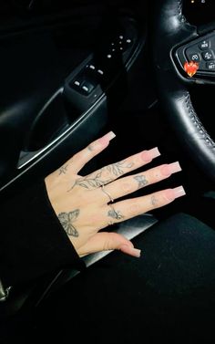 a woman's hand on the steering wheel of a car, with tattoos on her fingers