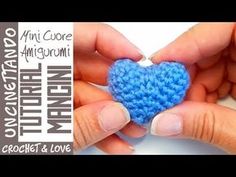 two hands holding a small blue crochet heart in front of a white background