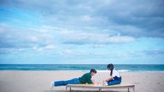 two people sitting on top of a beach next to the ocean